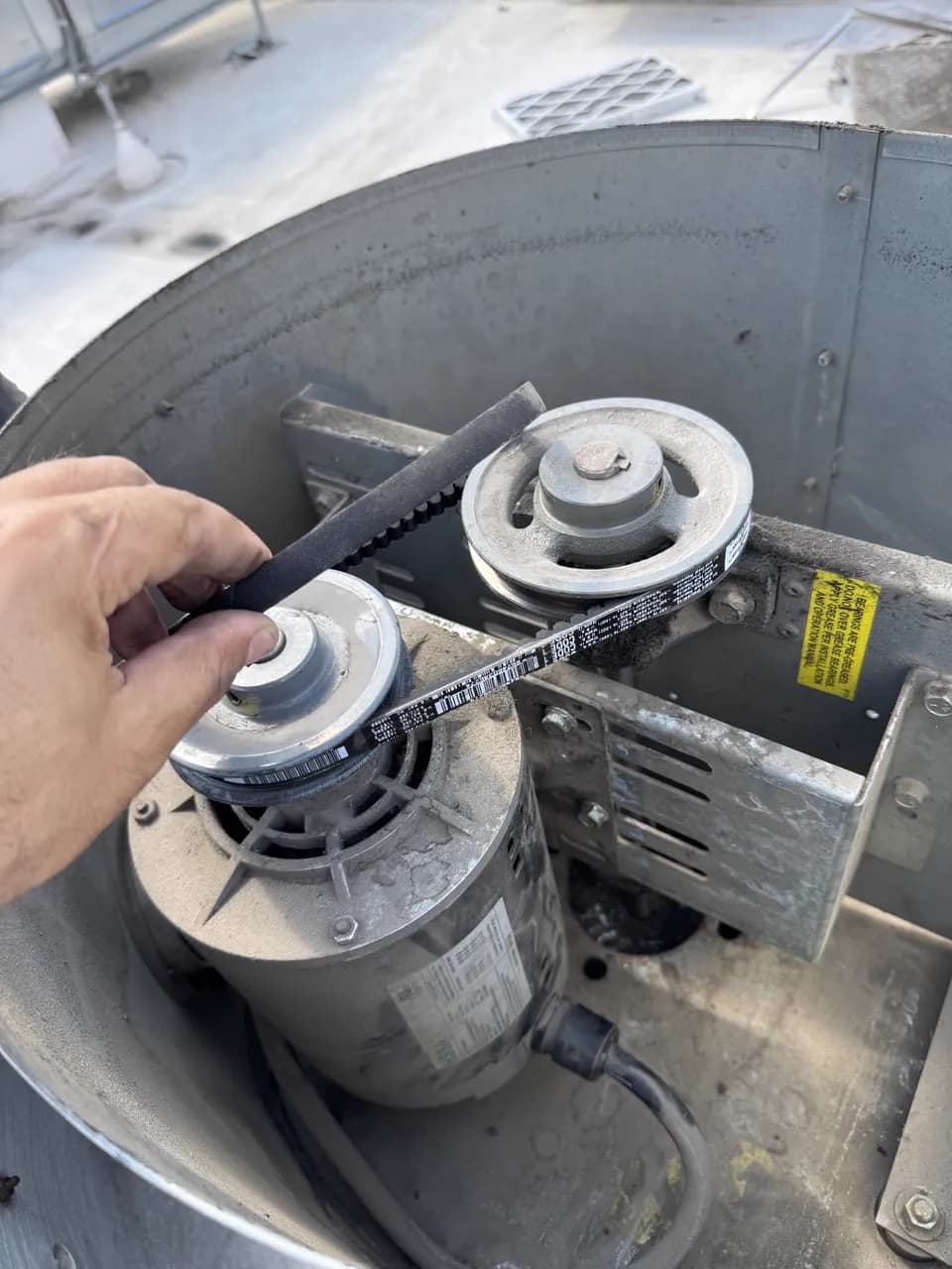 A technician's hand on the blower belt and pulleys of a rooftop unit