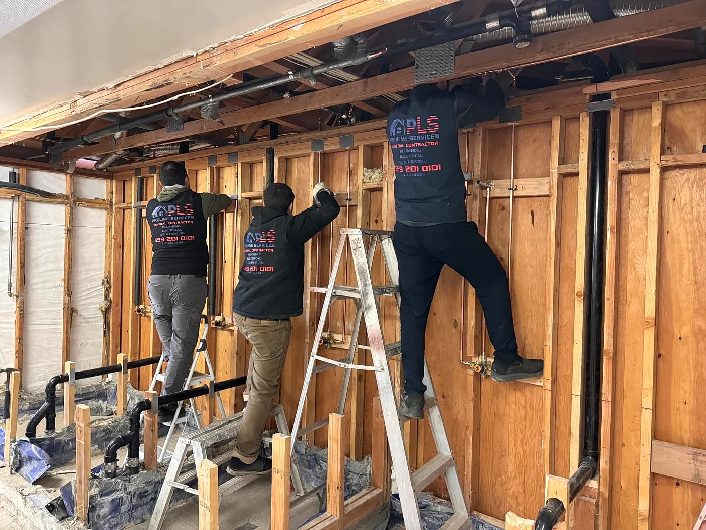 Three ProLine crew members working on ladders in an opened commercial wall