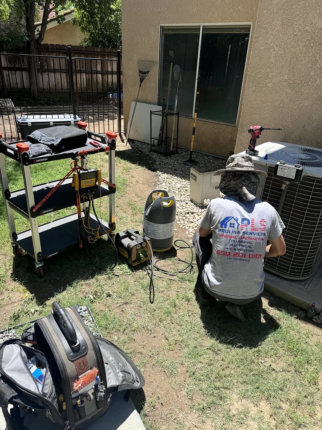 A ProLine technician kneeling at an outdoor AC unit with tools and a recovery machine