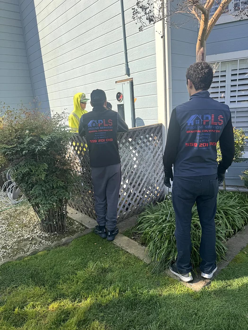 Two ProLine electricians on an outdoor electrical job beside a fence
