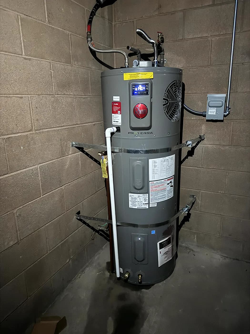 A new heat-pump water heater mounted against a block wall with new piping