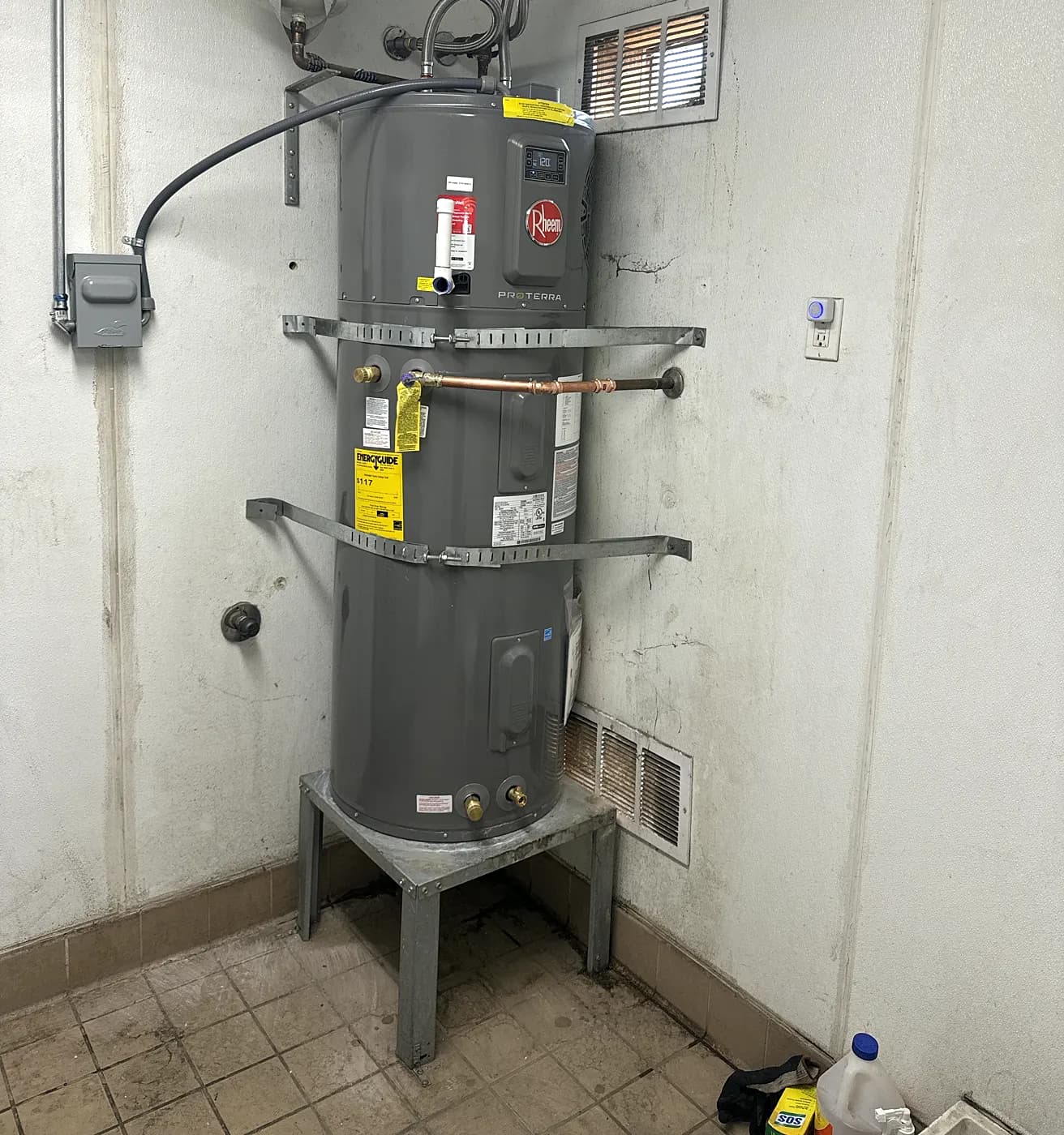 A new water heater on a stand with new piping in a laundry area